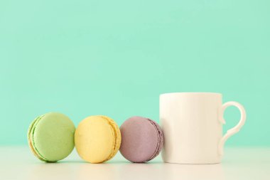 Beyaz kahve ve renkli badem kurabiyesi ya da pastel ahşap masanın üzerinde badem kurabiyesi.