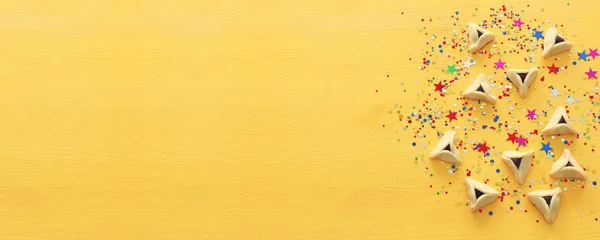 Concetto di celebrazione Purim (festa di carnevale ebraica). Biscotti Hamantaschen su sfondo di legno giallo con coriandoli — Foto Stock