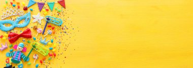 Parti renklendiricisi, maske ve sarı ahşap arka planda şirin bir palyaço bebeği. Üst manzara, düz uzanma