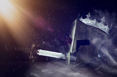 Kral şövalye miğferinin üzerinde taç ve karanlık arka planda kılıç resmi. Ortaçağ konsepti