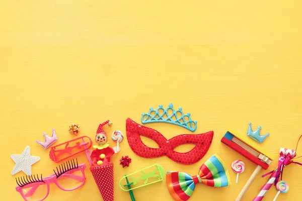 Party colorful noisemaker, mask and cute clown doll over yellow wooden background . Top view, flat lay — Stock Photo, Image