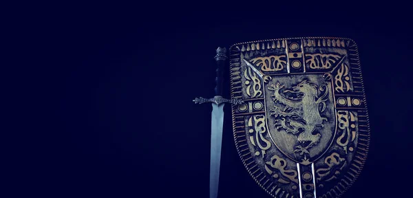 Foto de escudo caballero armadura y espada sobre fondo oscuro. Concepto de época medieval — Foto de Stock