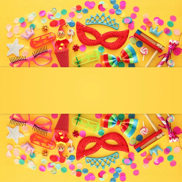 Party colorful noisemaker, mask and cute clown doll over yellow wooden background . Top view, flat lay — Stock Photo, Image