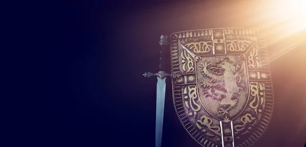 Foto de escudo cavaleiro armadura e espada sobre fundo escuro. Conceito de período medieval — Fotografia de Stock