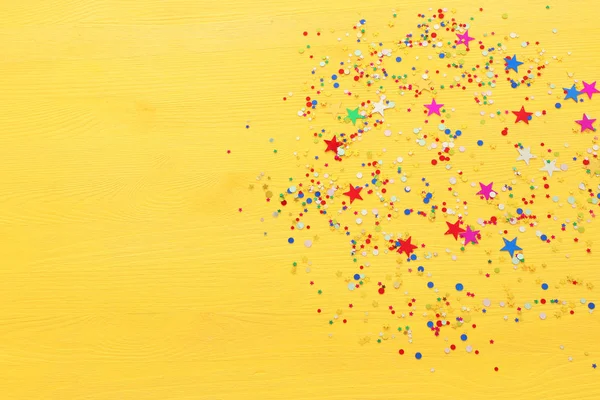 Party kleurrijke confetti over gele houten achtergrond. Bovenaanzicht, vlak lay — Stockfoto
