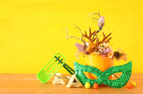 Purim viering beeld (joodse carnaval vakantie) met traditionele hamantasch cookies en herten gewei bloemdecoratie over gele houten achtergrond — Stockfoto