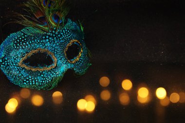 Zarif ve narin Venedik maskesinin fotoğrafı. Koyu parlak arka plan üzerinde tavus kuşu tüyleriyle kaplı.