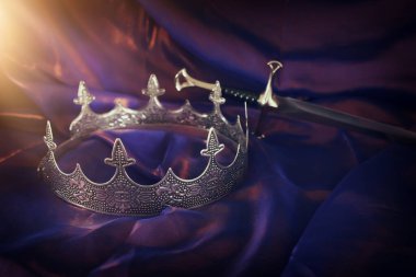 Güzel kraliçe / kral tacının sade görüntüsü ve koyu mor ipeğin üzerindeki kılıç. fantezi ortaçağ dönemi