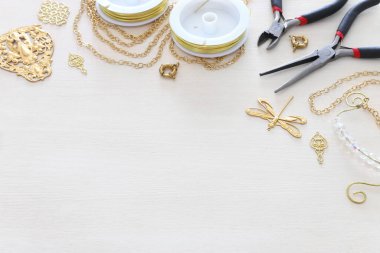 Altın zincir, filigran tılsımları ve beyaz ahşap arka planda aletlerle mücevher yapma kavramı