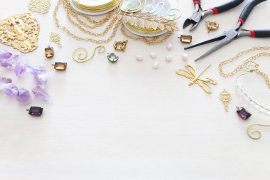Altın zincir, filigran tılsımları, inciler, jemler ve beyaz ahşap arka planda aletlerle mücevher yapma kavramı