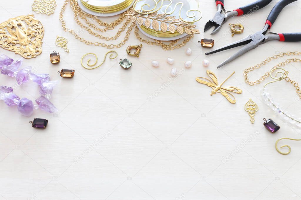 Jewellery making concept with gold chain, filigree charms, pearls, jems and tools over white wooden background