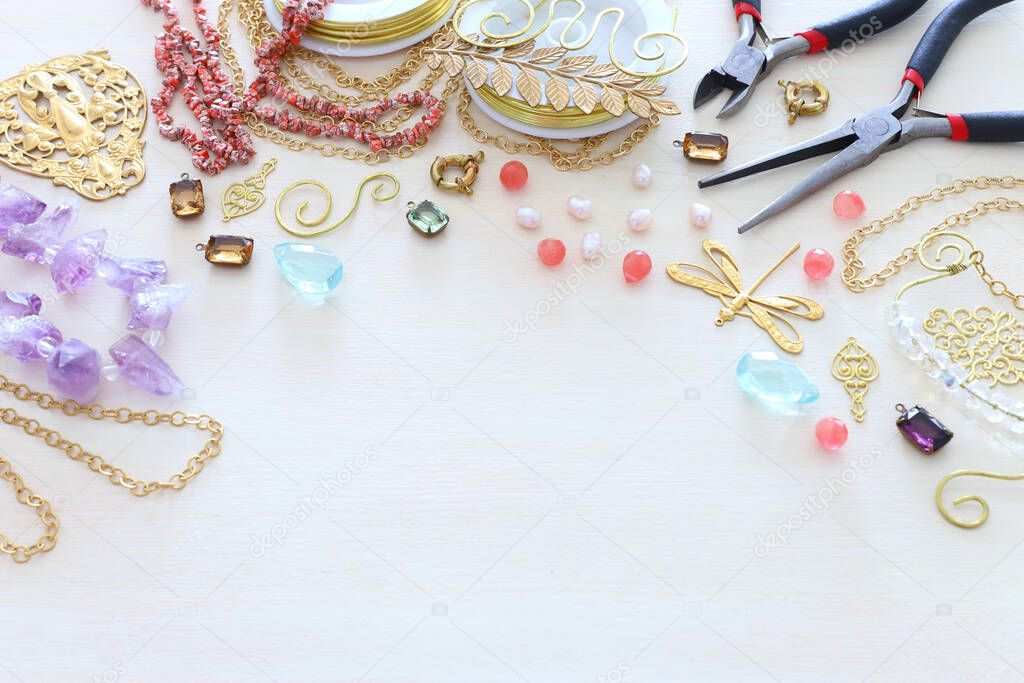 Jewellery making concept with gold chain, filigree charms, pearls, jems and tools over white wooden background