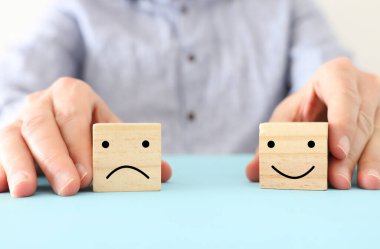 male hand holding wooden cube with sad face. concept of anxiety, stress or sad emotions clipart