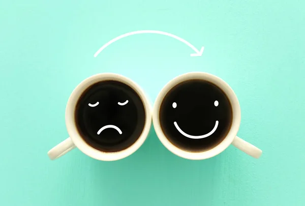 unhappy and happy smileys faces over cpffee cups. concept of mindset and emotions