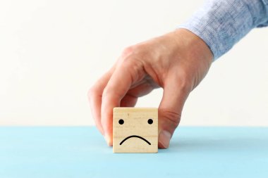 Erkek eli, üzgün suratlı tahta küpü tutuyor. Anksiyete, stres ya da hüzünlü duygular kavramı