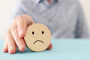 Erkek eli, üzgün suratlı tahta küpü tutuyor. Anksiyete, stres ya da hüzünlü duygular kavramı