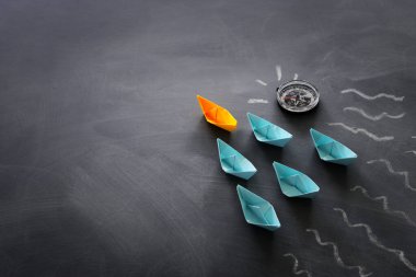 Karatahta arka planında kağıt tekne olan liderlik afişi konsepti. Bir lider gemi diğerlerine liderlik eder.