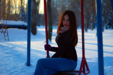 Kış akşamında bir kızın portresi. Kız salıncakta oturuyor