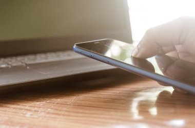Yakın plan iş adamı eli cep telefonu kullanıyor ve daktilo ediyor. Arka planda bilgisayar monitörü var. Modern işyerinde çalışan teknolojili iş adamları. İnternet konsepti. Seç