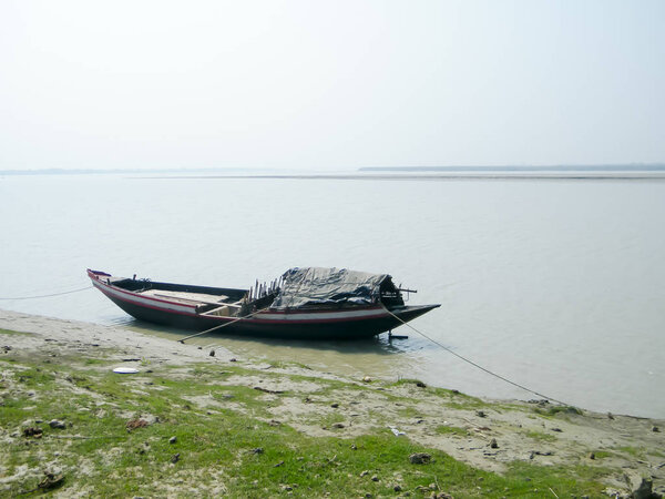 Narrow fishing boat (nautical vessel) floating on water on Ganges riverside coastal area near Bay of Bengal in evening. Rural india fishing village background scene. Sundarbans Mohona, West Bengal.
