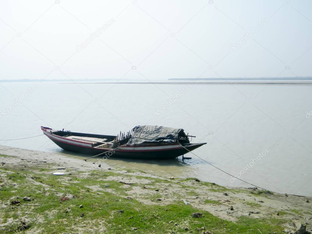 Narrow fishing boat (nautical vessel) floating on water on Ganges riverside coastal area near Bay of Bengal in evening. Rural india fishing village background scene. Sundarbans Mohona, West Bengal.