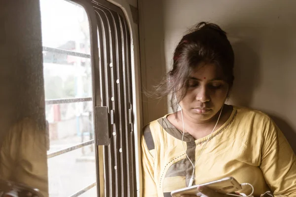 Mujer usando el teléfono móvil mientras viaja solo en tren de pasajeros. Viajero disfrutando de la tecnología moderna en movimiento en la vida cotidiana y los viajes. Retrato de cerca - Señora joven adulta - Etnia india . —  Fotos de Stock