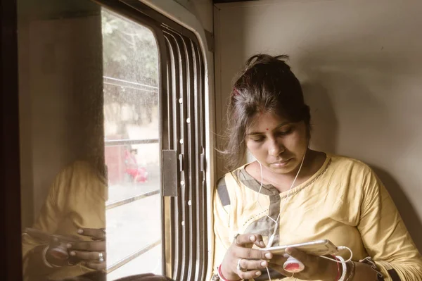 Mujer usando el teléfono móvil mientras viaja solo en tren de pasajeros. Viajero disfrutando de la tecnología moderna en movimiento en la vida cotidiana y los viajes. Retrato de cerca - Señora joven adulta - Etnia india . — Foto de Stock