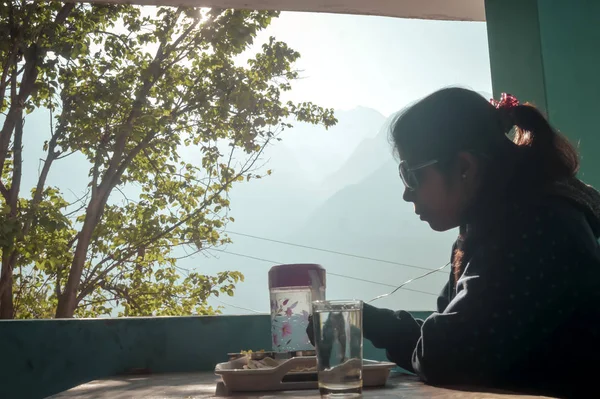 Donna che mangia facendo colazione seduta su un tavolo da pranzo al mattino nella casa di vacanza sullo sfondo delle montagne dell'Himalaya . — Foto Stock