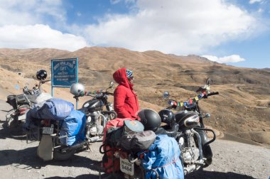 Motosikletinin yanında duran Hintli kadın gezgin ve bisikletçi Himalaya Dağları 'nda yürüyüş yapıyor ve yerel tepe istasyonunu keşfediyor. Macera Turizmi Takımı. Kaza Hindistan Ekim 2019