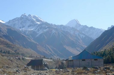 A mountain Alpine hut cabin in high Himalayas mountains, located to provide shelter to mountaineers, climbers and hikers. An interlocking overlapping spur hill ridges V-shaped valley in background. clipart