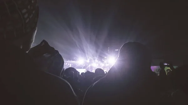 Силует великої аудиторії щасливих людей, що стоять на концертних майданчиках, підбадьорюють, використовують смартфони, піднімаючи руки вгору в повітрі перед музичним гуртом, насолоджуючись. Сценічне світлове відображення спереду . — стокове фото