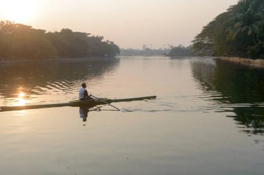 Individual Sports Speed Rower in Single scull crew rowing boat sliding racing shell on lake water oars in motion sitting sliding rigger seat doing exercise, fitness workout in sunset. Kolkata May 2019