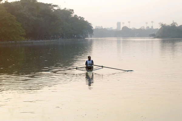 Individuele Sports Speed Rower in Single scull crew roeiboot glijden race shell op meer water roeispanen in beweging zitten glijdende rigger stoel doen oefening, fitness training bij zonsondergang. Kolkata mei 2019 — Stockfoto