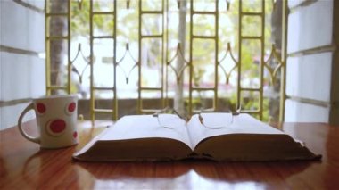 Açık bir kitap, kahve fincanı, gözlük ya da gözlük, sıcak güneşli bir sabah, yakın çekim. Eğitim ya da Tatil Konsepti. Seçici odak içinde izole arkaplan, alanın sığ derinliği
