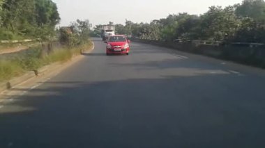 Güneşli bir günde hızlı giden araba şehir caddesinde kameraya yaklaşıyor. Arabanın arka koltuğundan arka manzara. Araba bakış açısı aracın arkasında. Kolkata Fab 2010