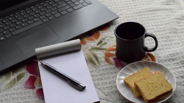 早餐咖啡在早上的阳光下 笔记本电脑黑色的钢笔和白色的条纸笔记本 陶瓷杯茶托和饼干在办公室顶部的工作台背景 生活方式形象 — 图库视频影像