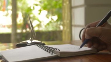 İş adamının eli kalemle kapanıyor ve ofis masasında kişisel ajandaya bazı finansal rakamlar yazıyor. Cep telefonunun odak arkaplanı dışında. Planlama ve evrak arkaplan hareketli resim