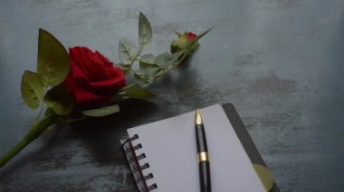 Boş Sayfa Defteri, kalem ve kırsal metal zemin üzerinde kopyalanmış güzel kırmızı bir gül. Aşk mektubu yazma ya da sevgililer günü düğünü ve tatilleri için evlenme teklifi. Üst görünüm.