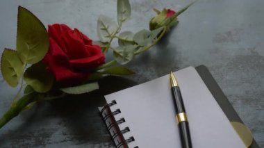 Boş Sayfa Defteri, kalem ve kırsal metal zemin üzerinde kopyalanmış güzel kırmızı bir gül. Aşk mektubu yazma ya da sevgililer günü düğünü ve tatilleri için evlenme teklifi. Üst görünüm.