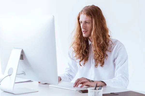 Homem de negócios tatuado elegante com gengibre cabelo longo trabalhando com computador no espaço de trabalho — Fotografia de Stock