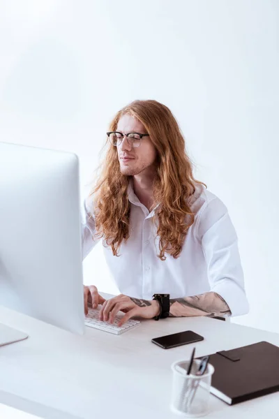 Stylischer tätowierter Geschäftsmann mit lockigem Haar, der im Büro am Computer arbeitet — Stockfoto