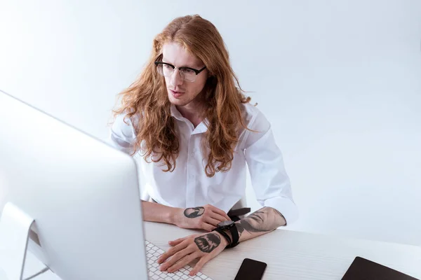 High angle view of stylish tattooed businessman with curly hair looking at computer in office — Stock Photo