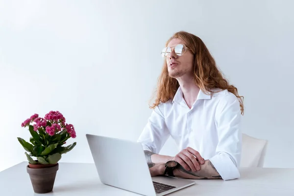 Homem de negócios tatuado elegante com cabelo encaracolado sentado à mesa com laptop e olhando para cima — Fotografia de Stock