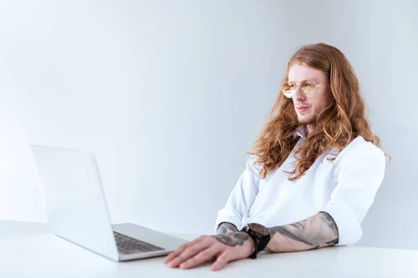 Side view of stylish tattooed businessman with curly hair looking at laptop — Stock Photo