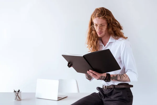 Homem de negócios tatuado elegante com cabelo encaracolado sentado na mesa e ler documentos no local de trabalho — Fotografia de Stock