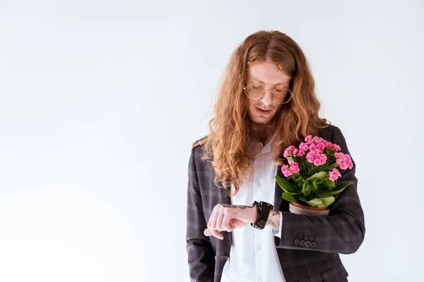 Stylish tattooed businessman with curly hair holding potted flowers and checking time isolated on white — Stock Photo