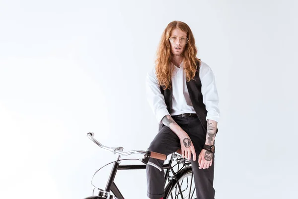 Stylische tätowierte Geschäftsmann mit langen Ingwerhaaren sitzt auf Fahrrad isoliert auf weiß — Stockfoto