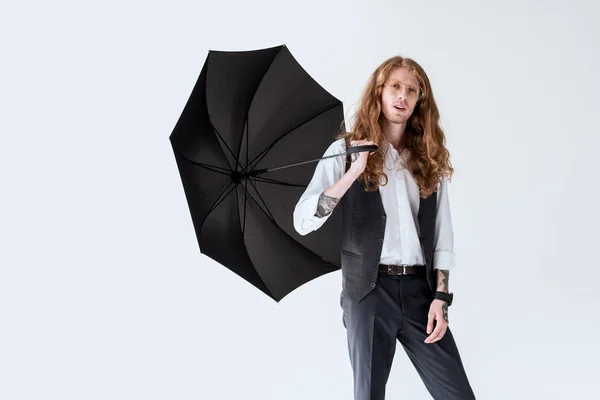 Hombre de negocios de moda con cabello de jengibre sosteniendo paraguas negro aislado en blanco - foto de stock