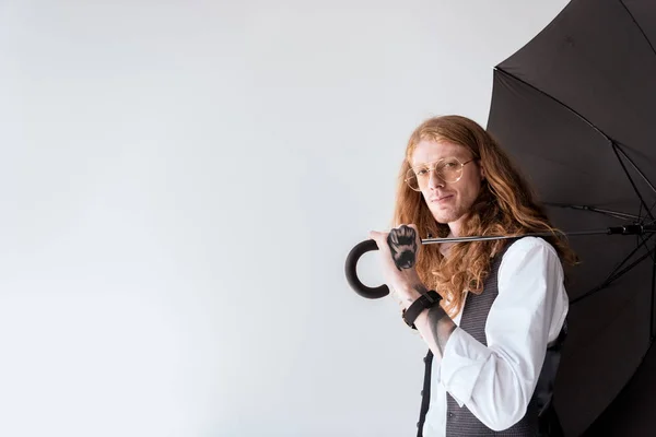 Seitenansicht von stilvollen tätowierten Geschäftsmann mit Ingwerhaaren hält schwarzen Regenschirm isoliert auf weiß — Stockfoto