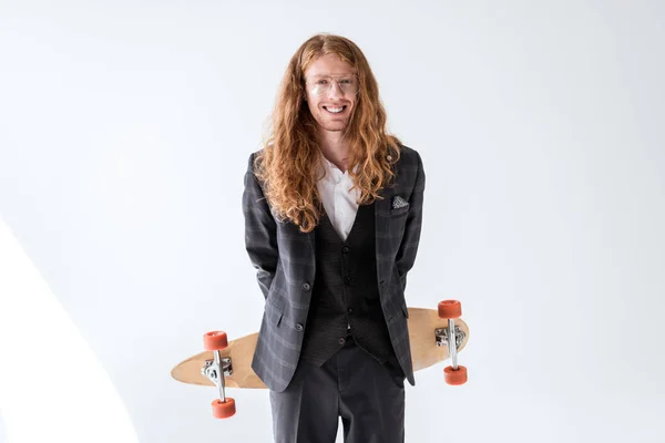 Sonriente hombre de negocios elegante con pelo rizado sosteniendo longboard por encima de la espalda - foto de stock